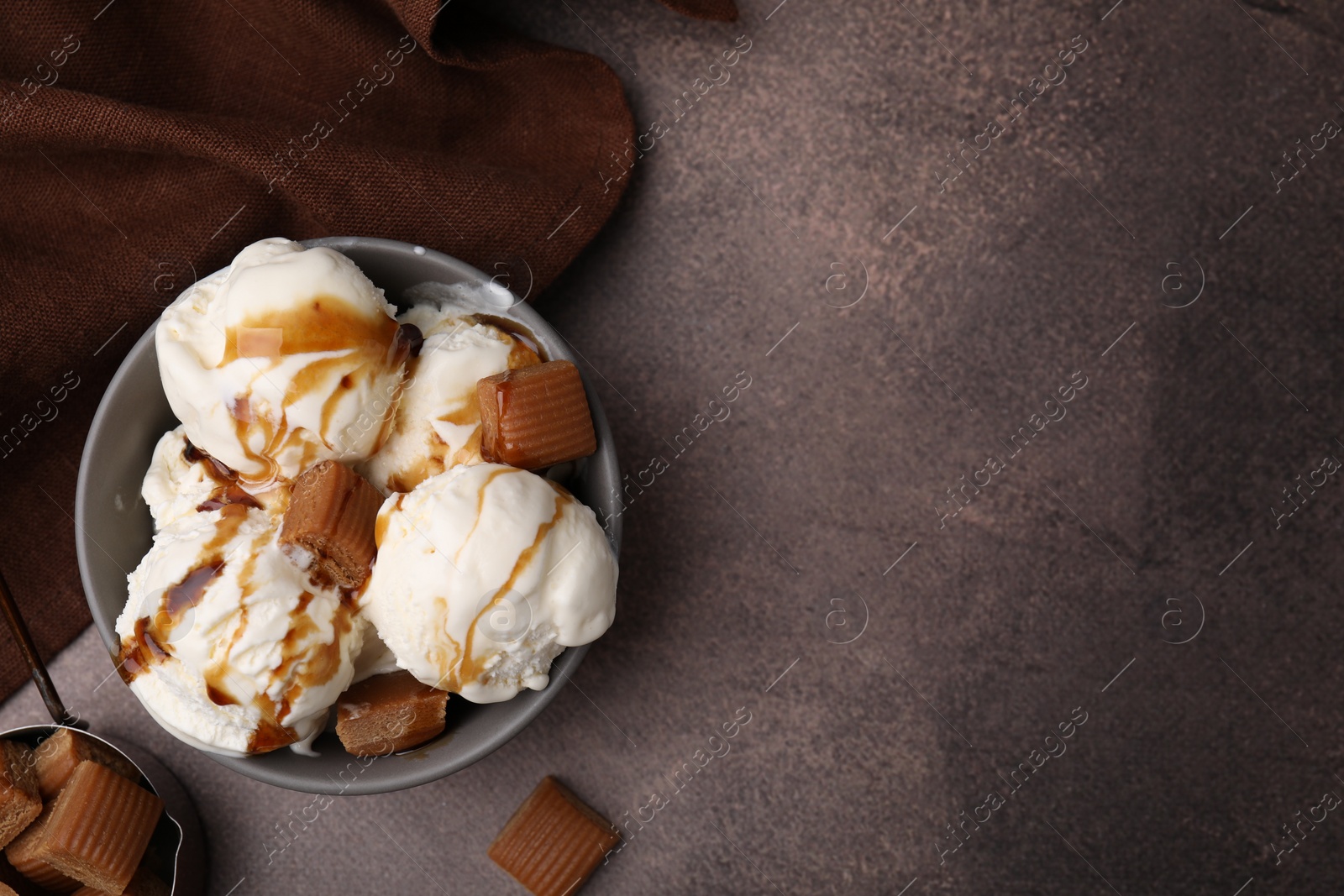Photo of Scoops of ice cream with caramel sauce and candies on textured table, flat lay. Space for text