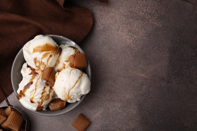 Scoops of ice cream with caramel sauce and candies on textured table, flat lay. Space for text