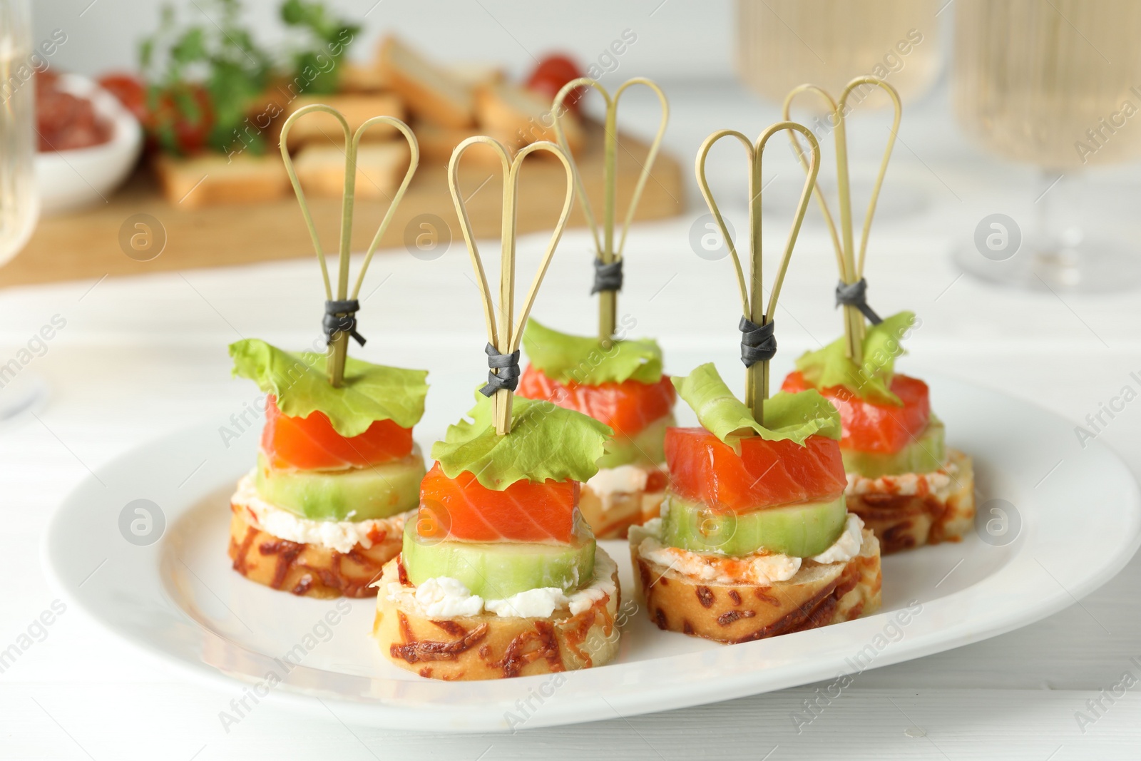 Photo of Tasty canapes with salmon, cucumber, bread and cream cheese on white wooden table, closeup