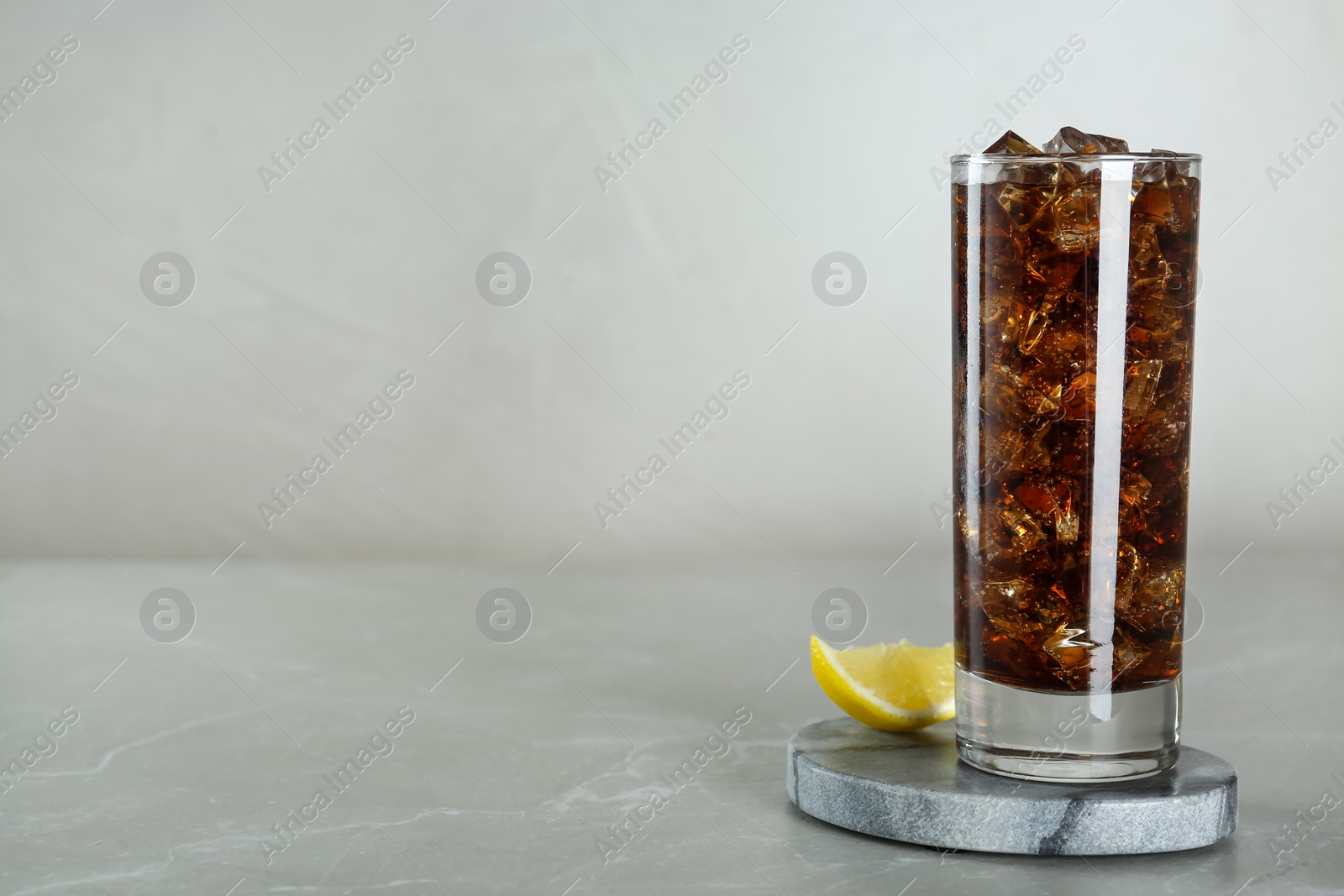 Photo of Glass of refreshing soda water with ice cubes and lemon on light grey table, space for text