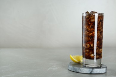 Glass of refreshing soda water with ice cubes and lemon on light grey table, space for text