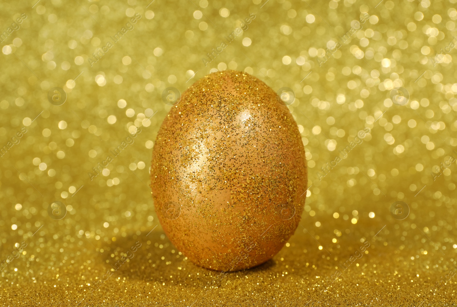 Photo of Shiny golden egg with glitter on yellow background, closeup