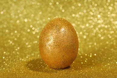 Photo of Shiny golden egg with glitter on yellow background, closeup