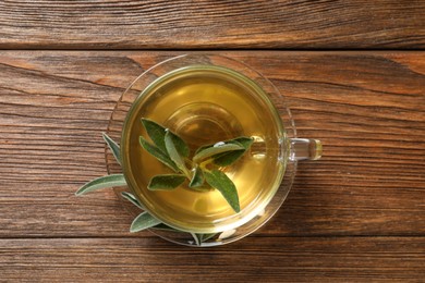 Photo of Cup of aromatic sage tea with fresh leaves on wooden table, top view