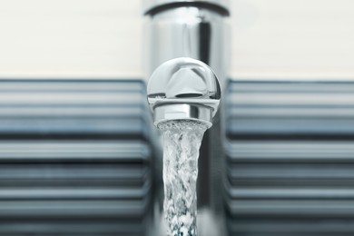 Water flowing from tap on blurred background, closeup