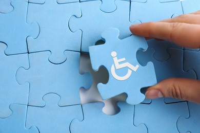 Image of Inclusion concept. Woman putting light blue puzzle with international symbol of access together, closeup