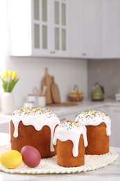 Photo of Delicious Easter cakes with sprinkles and painted eggs on white table in kitchen