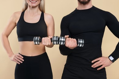 Athletic people exercising with dumbbells on light brown background, closeup