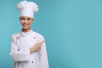 Photo of Happy woman chef in uniform pointing at something on light blue background, space for text