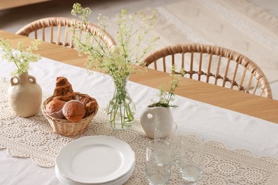 Photo of Clean dishes, flowers and fresh pastries on table in stylish dining room