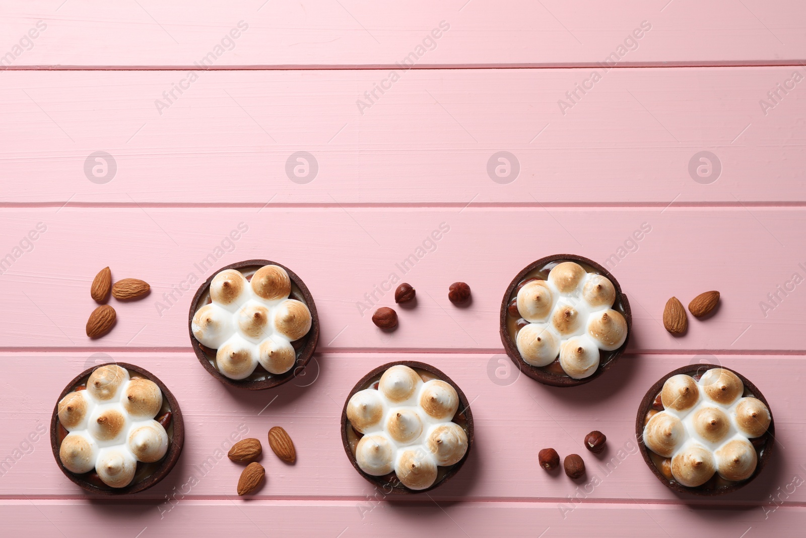 Photo of Salted caramel chocolate meringue tarts and nuts on pink wooden table, flat lay. Space for text
