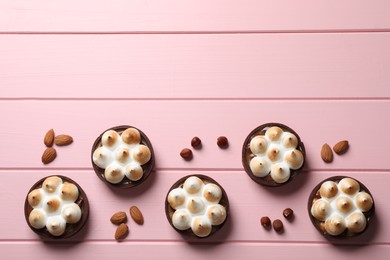 Photo of Salted caramel chocolate meringue tarts and nuts on pink wooden table, flat lay. Space for text