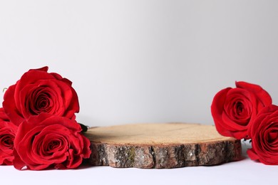 Presentation for product. Wooden podium and beautiful red roses on light background, space for text