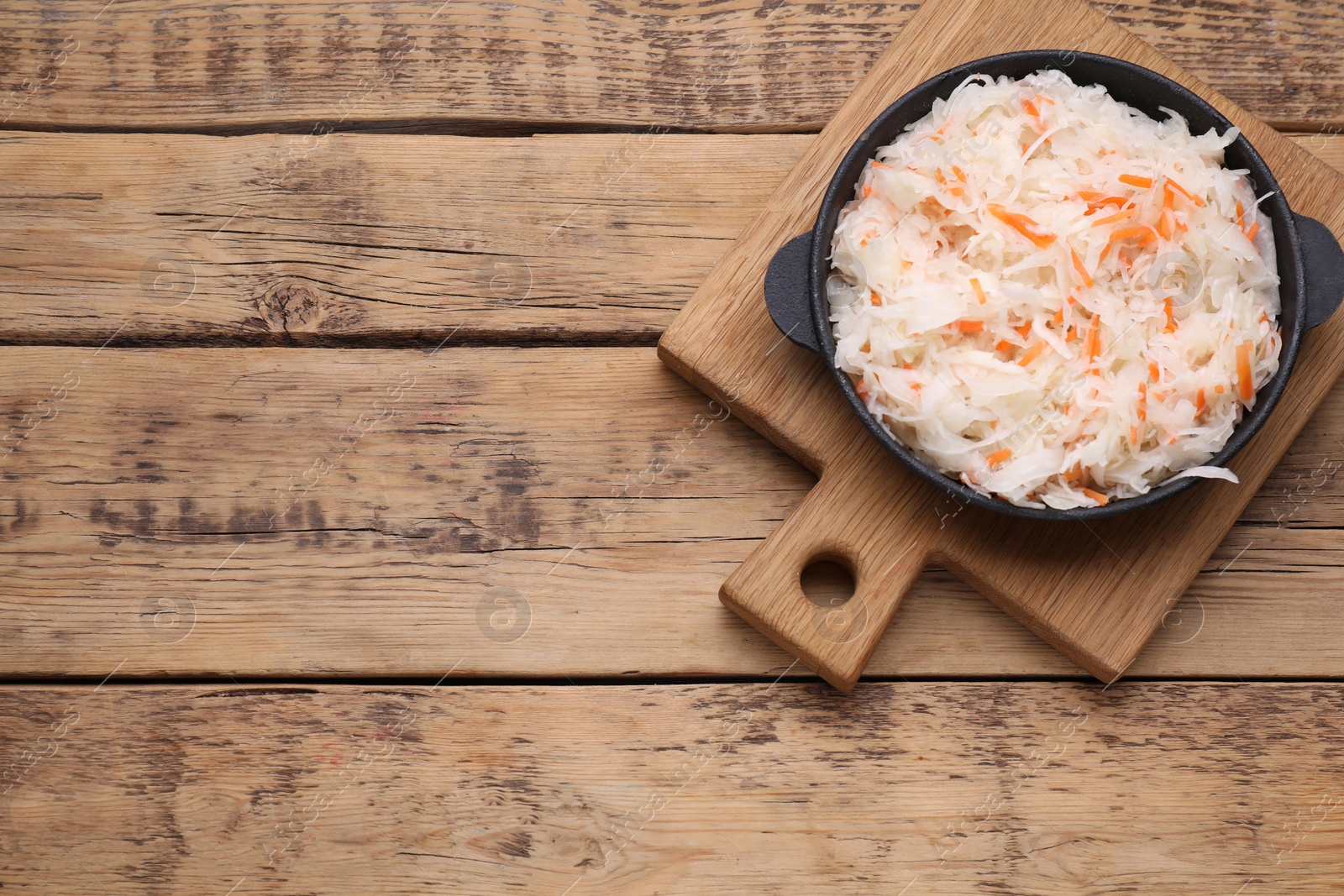 Photo of Bowl of tasty sauerkraut on wooden table, top view. Space for text