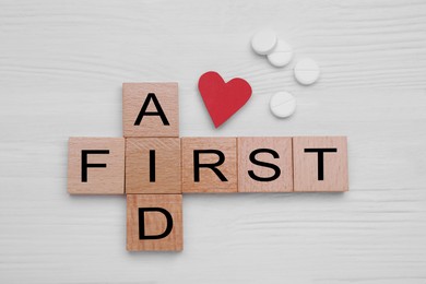 Photo of Words First Aid made of cubes, cardboard heart and pills on white wooden table, flat lay