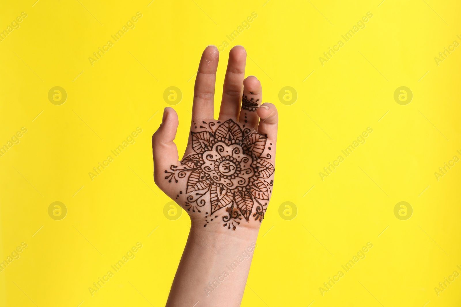 Photo of Woman with henna tattoo on palm against yellow background, closeup. Traditional mehndi ornament