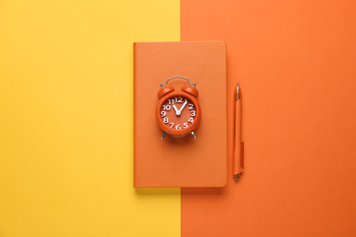 Image of Orange notebook, alarm clock and pen on color background, top view