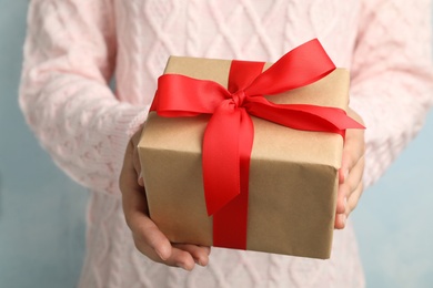 Woman holding beautiful Christmas gift on light blue background, closeup