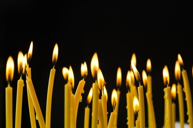 Many burning church candles on black background