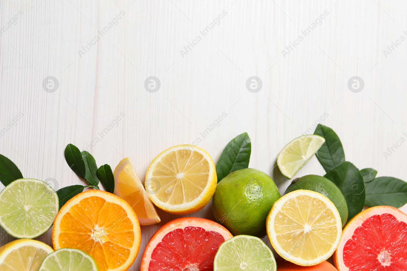 Photo of Different cut and whole citrus fruits on white wooden table, top view. Space for text