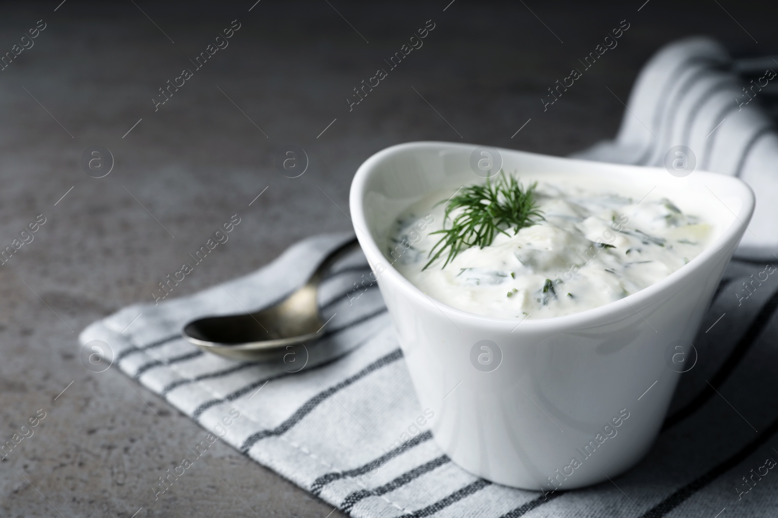 Photo of Cucumber sauce in ceramic bowl and spoon on grey background, space for text. Traditional Tzatziki