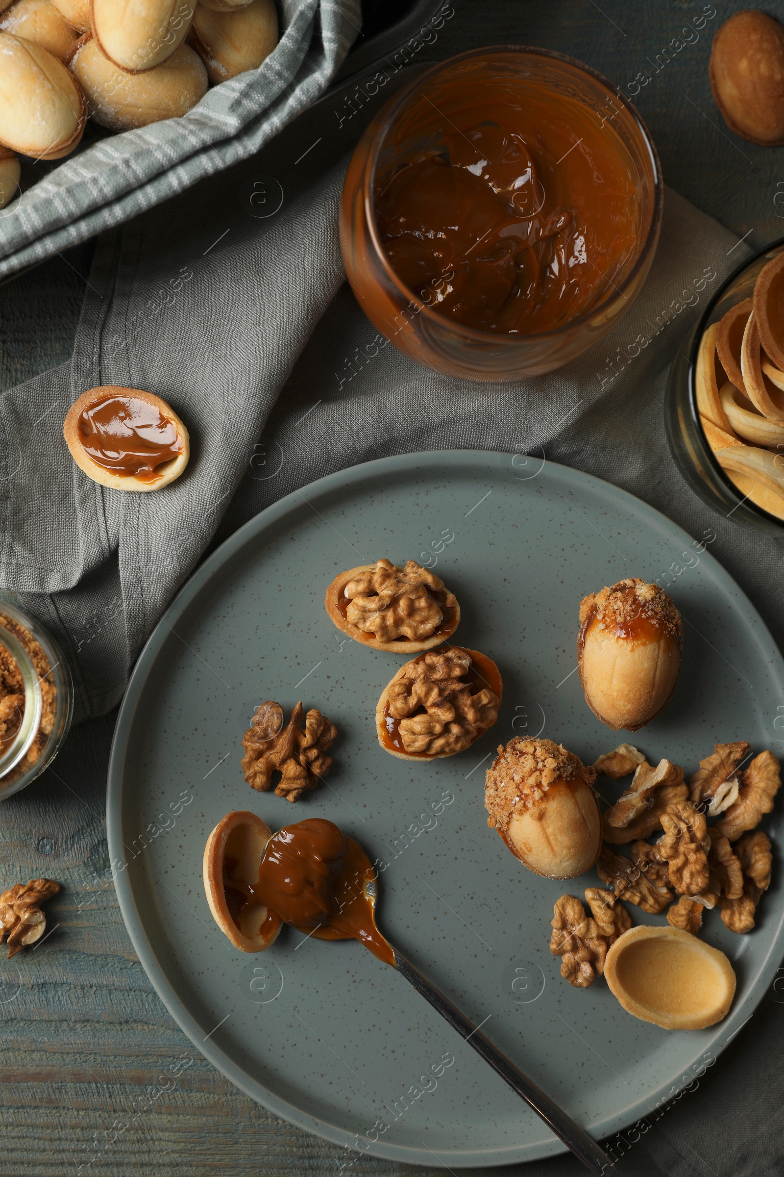 Photo of Freshly baked homemade walnut shaped cookies and boiled condensed milk on wooden table, flat lay