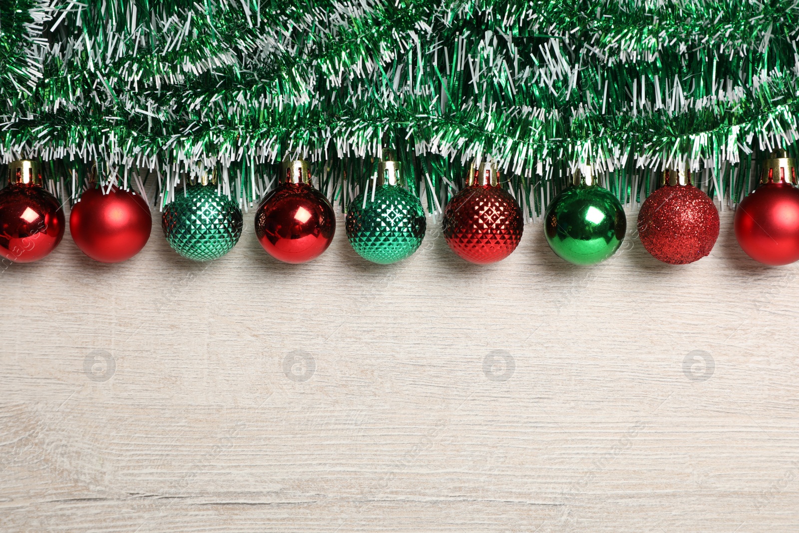 Photo of Green tinsel and Christmas balls on white wooden background, flat lay. Space for text