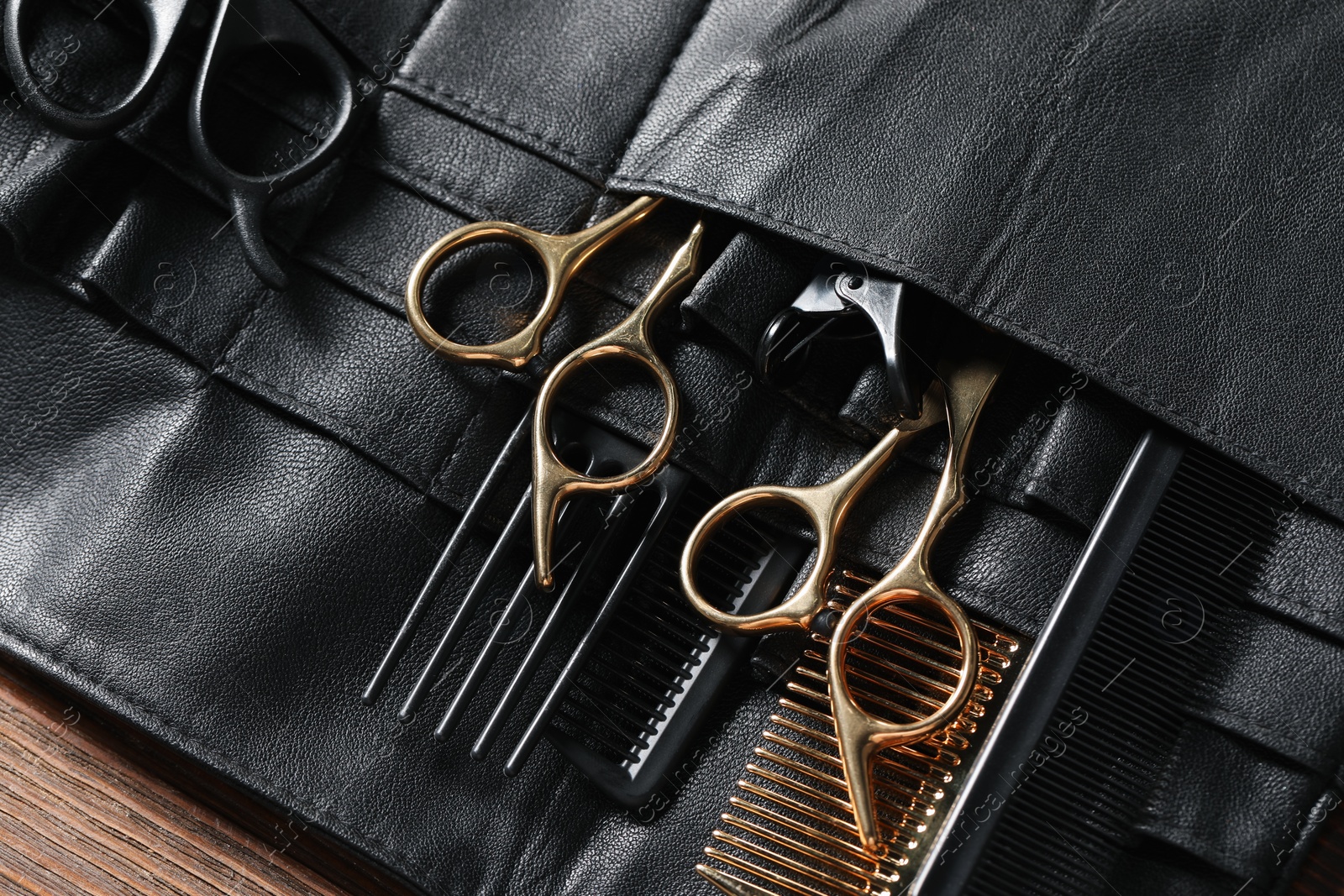 Photo of Hairdresser tools. Professional scissors and combs in leather organizer on wooden table, closeup