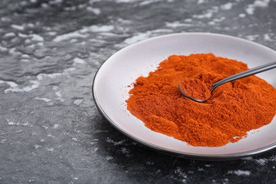 Photo of Plate of aromatic paprika on black textured table, closeup. Space for text