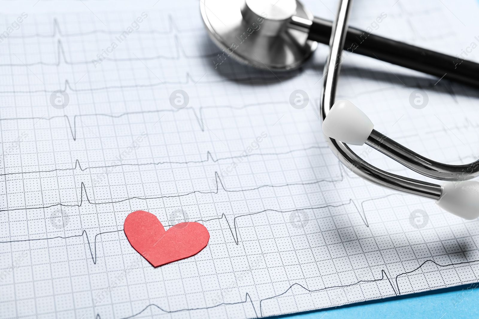 Photo of Cardiogram report with red paper heart and stethoscope on light blue background, closeup