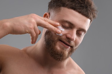 Photo of Handsome man applying moisturizing cream onto his face on grey background
