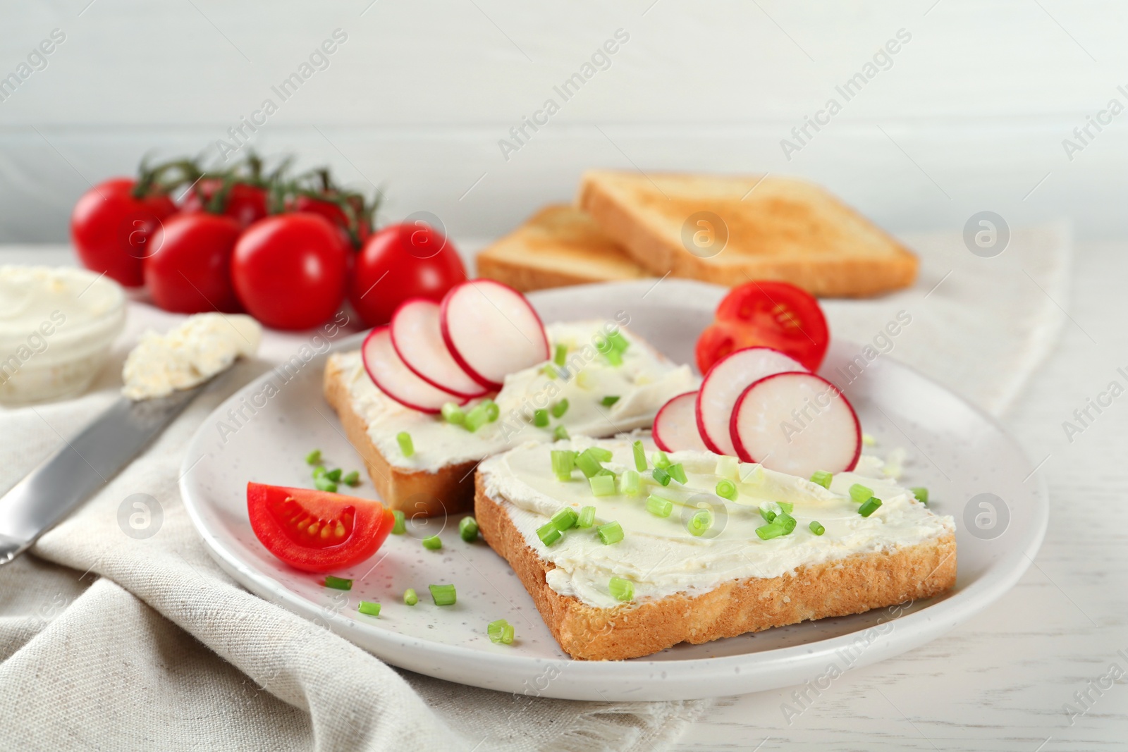 Photo of Toasted bread with cream cheese and vegetables on white wooden table