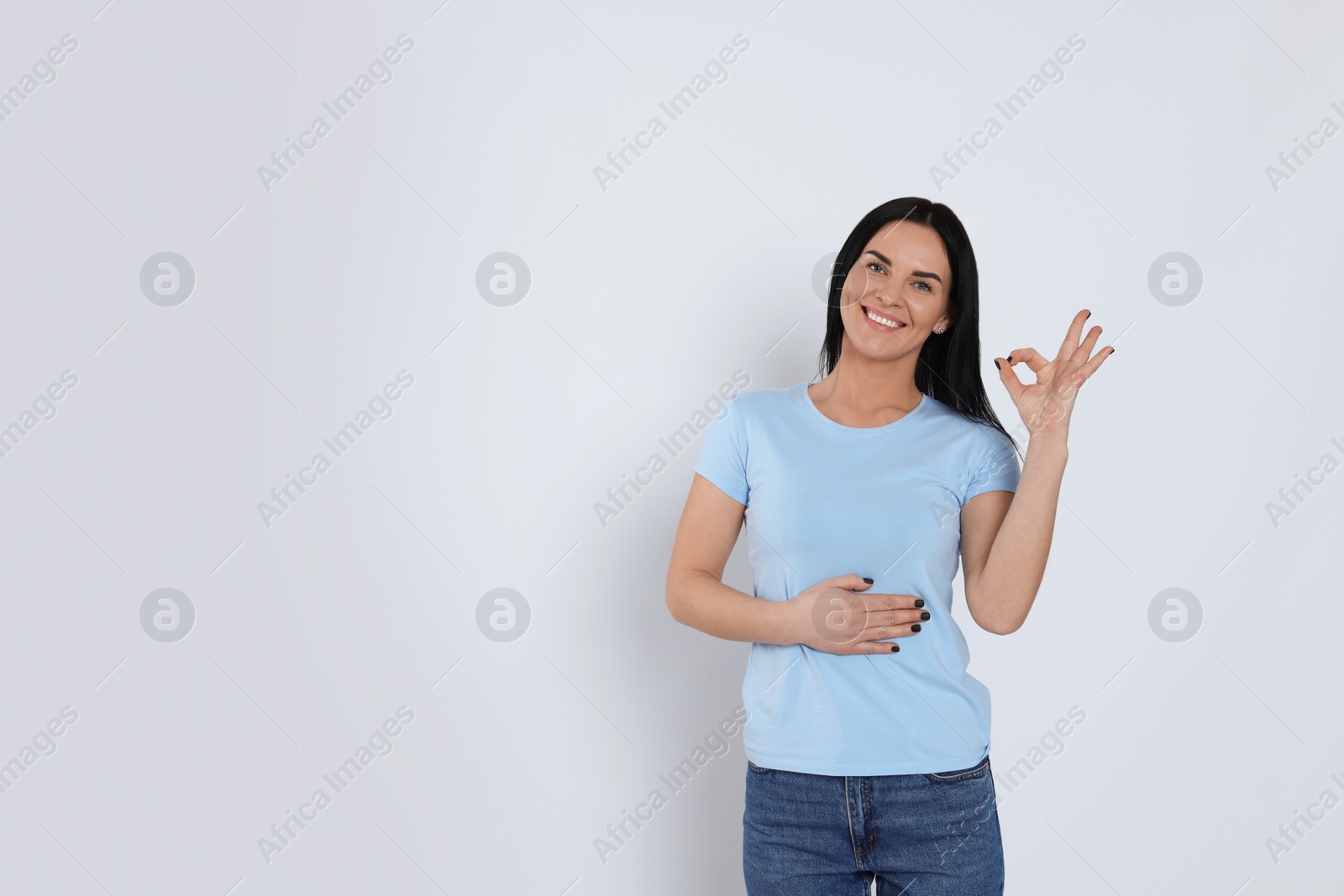 Photo of Happy woman touching her belly and showing okay gesture on light background, space for text. Concept of healthy stomach