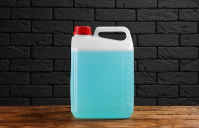 Photo of Plastic canister with blue liquid on wooden table against dark brick wall