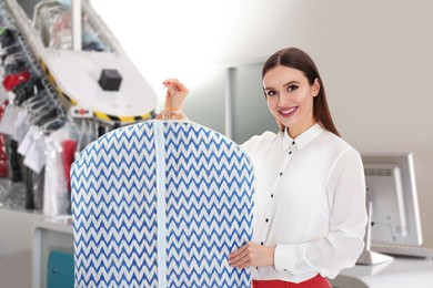 Image of Young woman holding hanger with clothes in garment cover indoors. Dry-cleaning service
