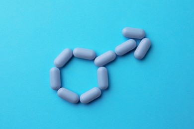 Photo of Male sign made of pills on light blue background, top view. Potency problem