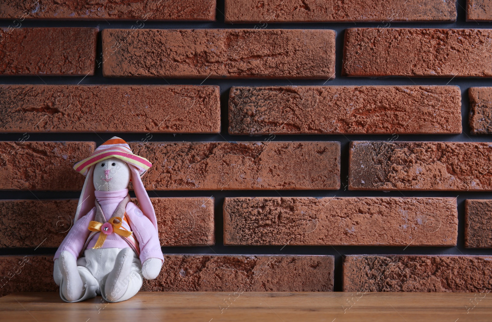 Photo of Abandoned toy bunny on table against brick wall background. Time to visit child psychologist