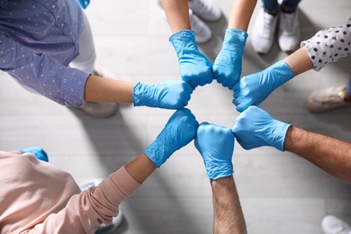Photo of People in blue medical gloves joining fists indoors, top view