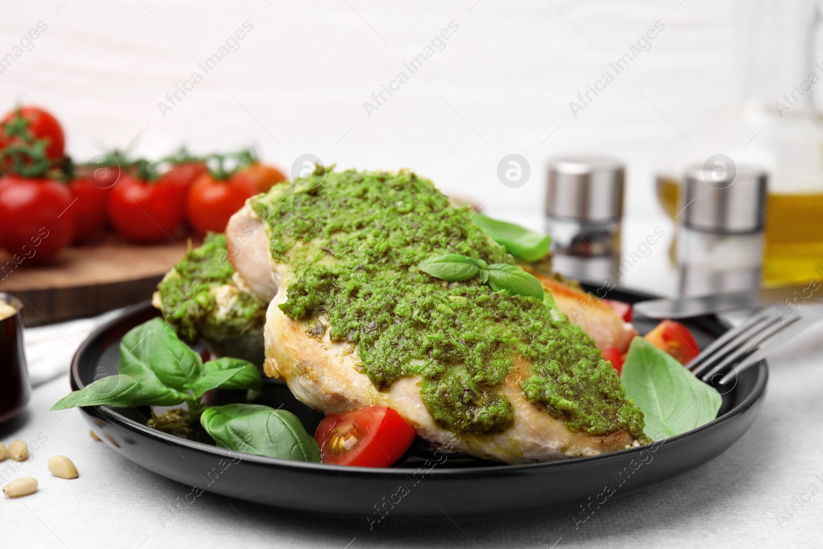 Photo of Delicious chicken breasts with pesto sauce, tomatoes and cutlery served on light table, closeup