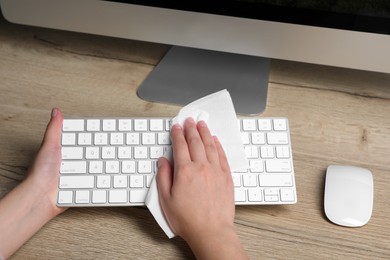Photo of Woman wiping keyboard with paper towel at wooden table, closeup