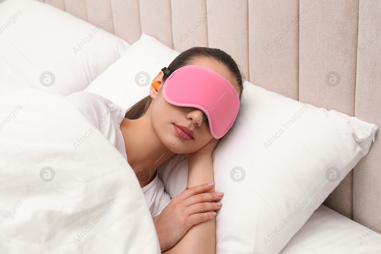Photo of Young woman with foam ear plugs and mask sleeping in bed