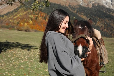 Photo of Young woman hugging horse in mountains on sunny day. Beautiful pet