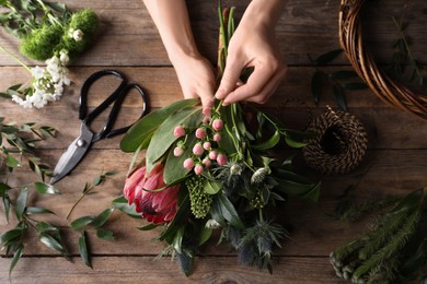 Florist making beautiful bouquet with fresh flowers at wooden table, top view