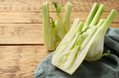 Photo of Whole and cut fennel bulbs on wooden table, closeup. Space for text