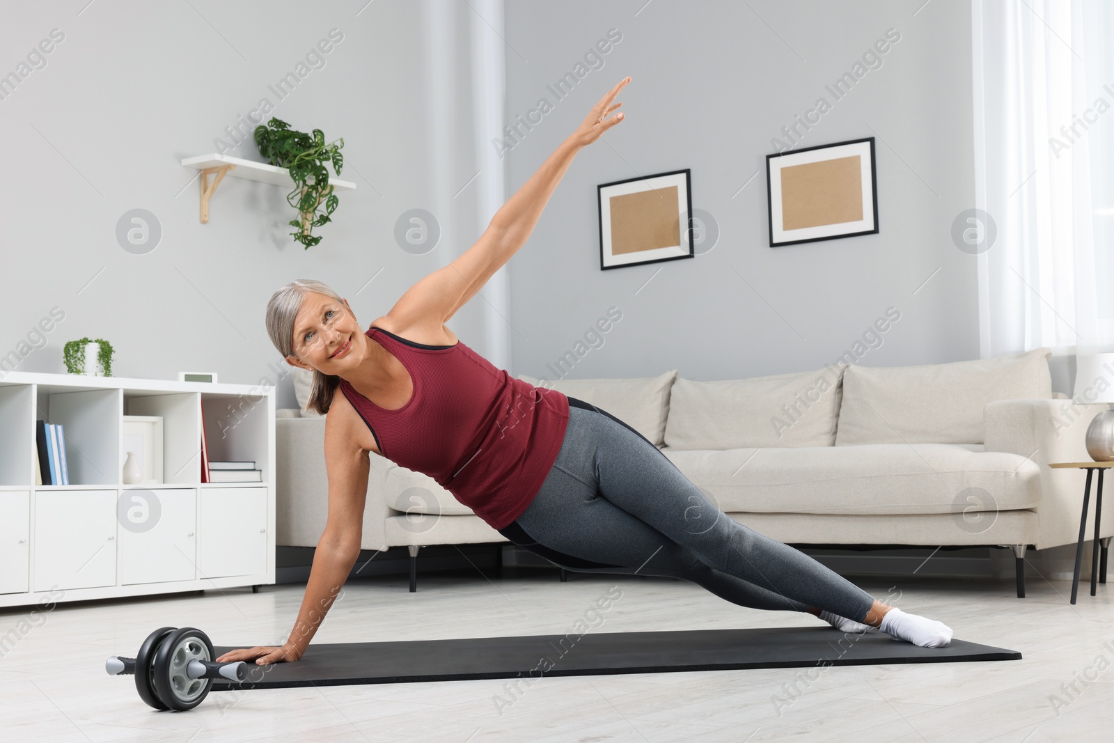 Photo of Senior woman in sportswear doing exercises on fitness mat at home