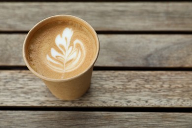 Takeaway paper cup with coffee on wooden table, above view. Space for text