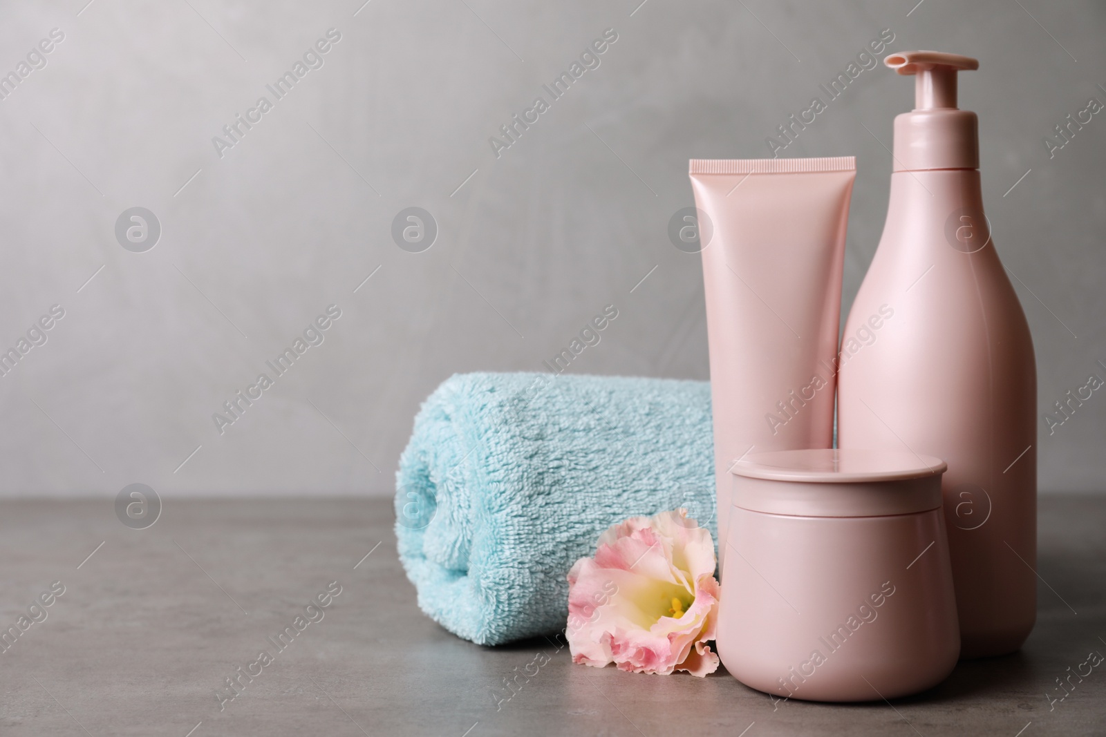 Photo of Different hair products, towel and flower on grey table. Space for text