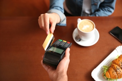 Woman using terminal for credit card payment in cafe, closeup