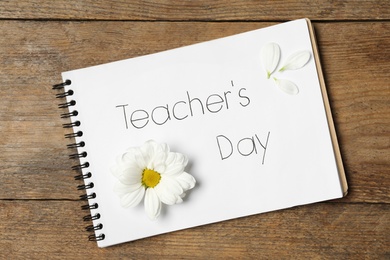 Notebook with words TEACHER'S DAY and beautiful flower on wooden table, top view