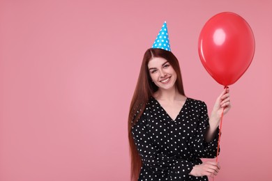 Happy woman in party hat with balloon on pink background, space for text